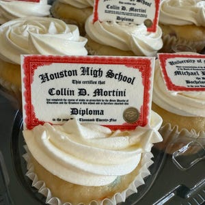 Może przedstawiać: Babeczki z białym lukrem, każda zwieńczona jadalnym obrazkiem w kształcie dyplomu. Na dyplomach widnieje napis "Houston High School" i "Collin D. Mortini". Babeczki znajdują się w przezroczystym plastikowym pojemniku.