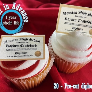 May include: Two cupcakes with white frosting and red swirls, each topped with a diploma. The diplomas read "Houston High School" and "Kayden Crawford." Text on the image says "Order in Advance" and "1 year shelf life."