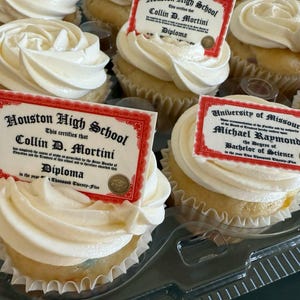 May include: A tray of cupcakes with white frosting, each topped with a diploma-shaped edible image. The diplomas read "Houston High School" and "University of Missouri", with names and degree information.