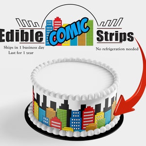 May include: A white cake with a city skyline edible image on the bottom tier. The image is colorful and features red, yellow, blue, and green buildings. The cake is decorated with white frosting and a white border. The text "Edible Comic Strips" is at the top of the image.