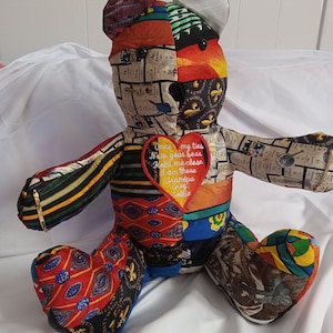 May include: A patchwork teddy bear made from colorful fabric scraps. The bear has a red heart on its chest with the embroidered text "Once my ties now your bear hold me close I am there Grandpa Greg Sallie".