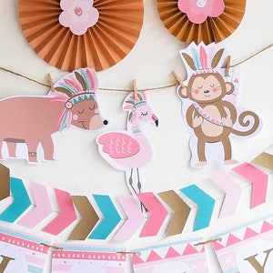 May include: A pink, blue, and gold banner with the word "Lucy" in gold letters. The banner is decorated with arrows, geometric patterns, and animal illustrations. The animals include a bear, a flamingo, and a monkey, all wearing headdresses with feathers. The banner is strung with twine and has wooden clothespins.