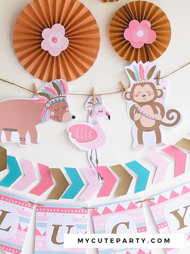 May include: A pink, blue, and gold banner with the word "Lucy" in gold letters. The banner is decorated with arrows, geometric patterns, and animal illustrations. The animals include a bear, a flamingo, and a monkey, all wearing headdresses with feathers. The banner is strung with twine and has wooden clothespins.