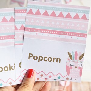 May include: Pink and green patterned table cards with gold text. The cards say "Popcorn" and "Cookies". The cards feature a pink owl with feathers and closed eyes.