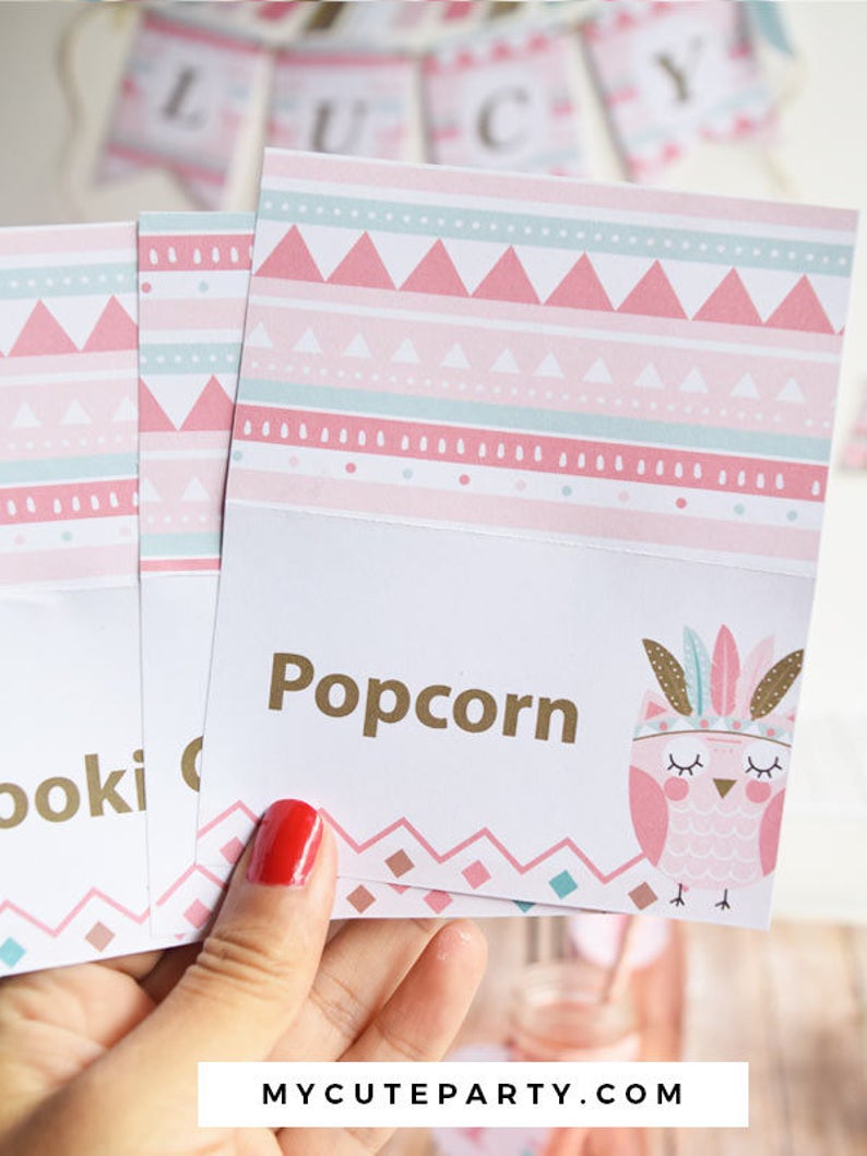 May include: Pink and green patterned table cards with gold text. The cards say "Popcorn" and "Cookies". The cards feature a pink owl with feathers and closed eyes.