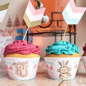 May include: Pink and blue cupcakes with animal-themed wrappers. The wrappers feature a squirrel and a monkey wearing a headdress. The cupcakes are topped with pink and blue frosting. The cupcakes are decorated with small arrows.