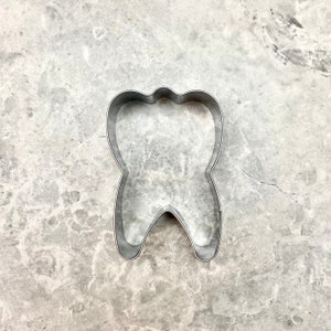 May include: A silver metal cookie cutter shaped like a tooth.