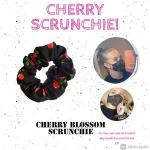 Könnte beinhalten: Ein schwarzes Haargummi mit Kirschendruck. Das Haargummi ist in einer Nahaufnahme abgebildet. Der Text "CHERRY SCRUNCHIE!" befindet sich oben im Bild. Der Text "CHERRY BLOSSOM SCRUNCHIE" befindet sich unten im Bild. Der Text "Ps. You can mix and match any mask & scrunchie for £71" befindet sich ebenfalls unten im Bild.