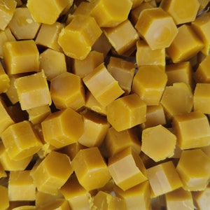 May include: A close-up of a pile of golden yellow beeswax blocks. The blocks are hexagonal in shape and have a smooth, shiny surface.