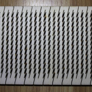 Puede incluir: Primer plano de una tabla de madera blanca con un patr&oacute;n repetitivo de l&iacute;neas en zigzag negras.