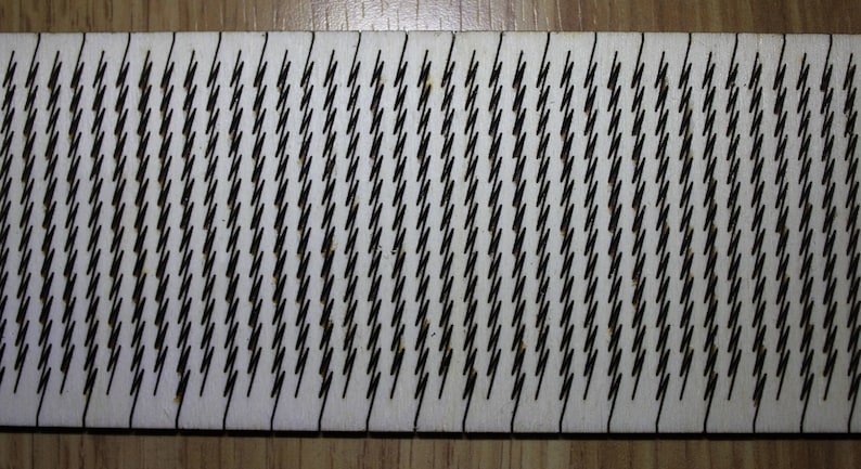 Puede incluir: Primer plano de una tabla de madera blanca con un patr&oacute;n repetitivo de l&iacute;neas en zigzag negras.