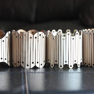 May include: Four wooden cylindrical containers with a decorative pattern of vertical lines and circles. The containers are made of light brown wood and have a slightly wavy shape.