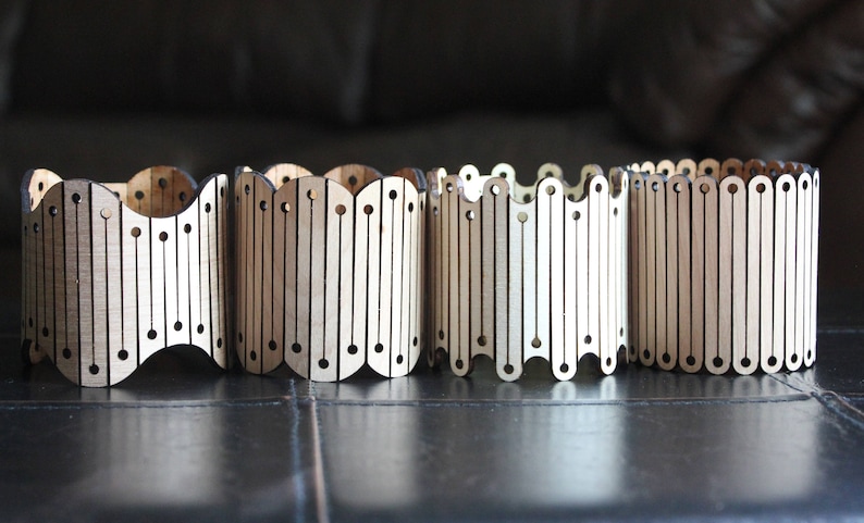 May include: Four wooden cylindrical containers with a decorative pattern of vertical lines and circles. The containers are made of light brown wood and have a slightly wavy shape.
