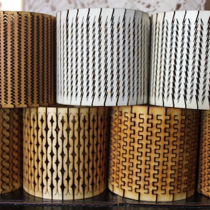 Puede incluir: Ocho portavelas de madera con diferentes patrones geom&eacute;tricos cortados con l&aacute;ser. Los portavelas est&aacute;n apilados en dos filas de cuatro. Los patrones incluyen zigzags, diamantes y cuadrados.