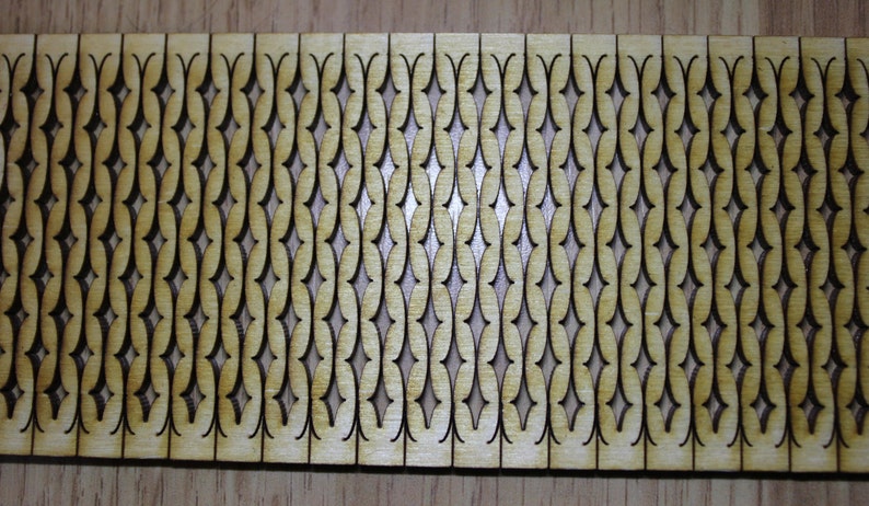 Puede incluir: Un panel de madera con un patr&oacute;n repetitivo de formas de diamante recortadas. El panel es de madera marr&oacute;n claro y los recortes son marr&oacute;n oscuro.