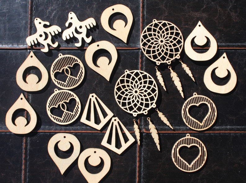 Op de afbeelding: Een verzameling onafgewerkte houten oorbelcomponenten in verschillende vormen. Ontwerpen omvatten druppels, halve manen, harten, geometrische vormen en dromenvangers met veervormige hangers. De stukken zijn lichtbruin en klaar voor personalisatie.