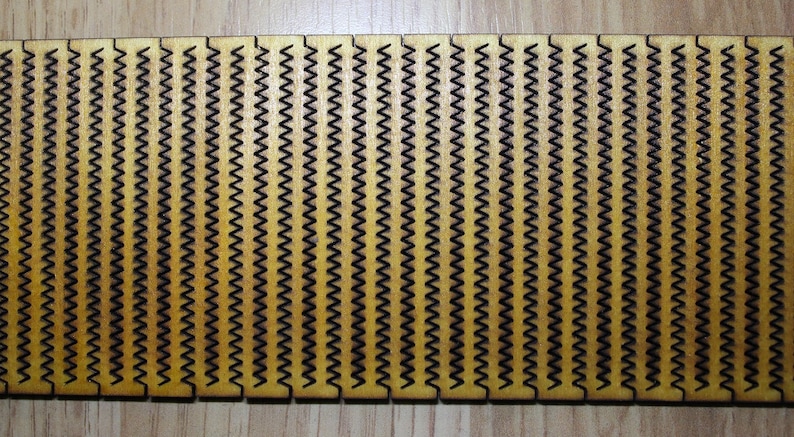 Puede incluir: Un panel de madera con un patr&oacute;n repetitivo de zigzags negros. El panel est&aacute; hecho de madera marr&oacute;n claro y tiene una superficie lisa.