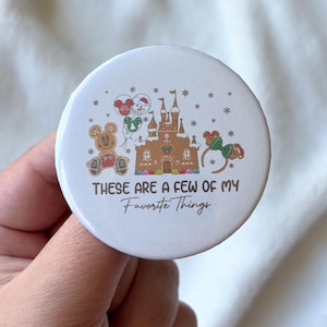 Puede incluir: Un botón blanco con el texto "These are a few of my Favorite Things". El botón presenta ilustraciones de un oso de jengibre, un castillo y orejas de Mickey Mouse. El botón es redondo y tiene un acabado brillante.