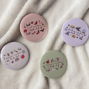 May include: Four circular badges with illustrations and text. The badges are for book clubs: "smut readers", "fantasy readers", "horror readers", and "romance readers". Each badge has a different colour and design, with small illustrations related to the book club themes.
