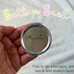 May include: A close-up of the back of a round button pin, held in a hand. The pin is silver with a safety pin clasp. The text "Button Back" is written in a colorful, cursive font. The text "This is an example, edge of back will match button" is also visible.