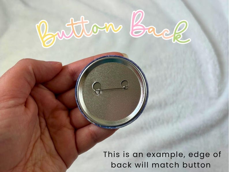 May include: A close-up of the back of a round button pin, held in a hand. The pin is silver with a safety pin clasp. The text "Button Back" is written in a colorful, cursive font. The text "This is an example, edge of back will match button" is also visible.