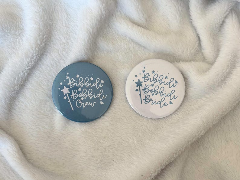 May include: Two round buttons with the text "Bibbidi Bobbidi Crew" and "Bibbidi Bobbidi Bride" in a whimsical font. The buttons feature a magic wand and star design. One button is blue, the other is white.