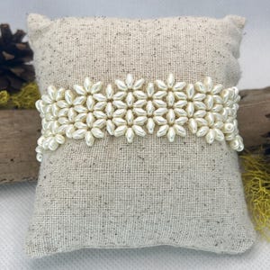 May include: A white pearl bracelet with a flower design. The bracelet is made of small, round pearls that are strung together in a pattern of flowers. The bracelet is on a white background.