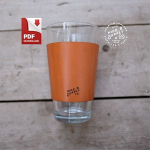 May include: A brown leather beer koozie with the text "HIDE & SUPPLY CO." printed on it. The koozie is on a glass beer mug.