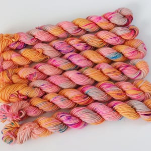 May include: A collection of colorful yarn skeins in shades of pink, orange, and yellow. The yarn is arranged in neat rows, showcasing the vibrant color variations. The skeins are tightly wound, suggesting a high-quality fiber for knitting or crochet projects.