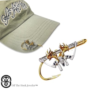 May include: Gold and silver deer head hat clip with a hook. The clip is shaped like a bow and arrow. The text "Off The Hook, Jeweler™" is visible in the image.