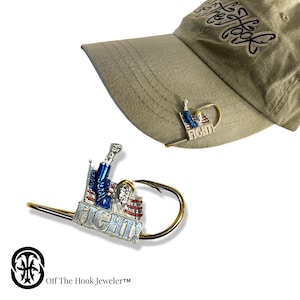 May include: A gold-colored fishing hook with a silver-colored figurine of a person holding a flag. The figurine is holding a fist in the air and the flag says "FIGHT!" The hook is attached to a brown baseball cap.