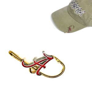 May include: A gold-colored metal key chain with a red and white letter "A" charm. The charm is attached to a gold-colored metal ring.