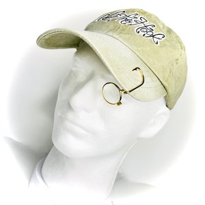 May include: A beige baseball cap with black embroidery that says "Coffee, then code". A gold-colored monocle is attached to the cap with a hook.