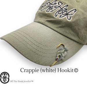 May include: A green baseball cap with the text "Off The Hook" embroidered on the front. A white crappie fish with a gold hook is attached to the cap.