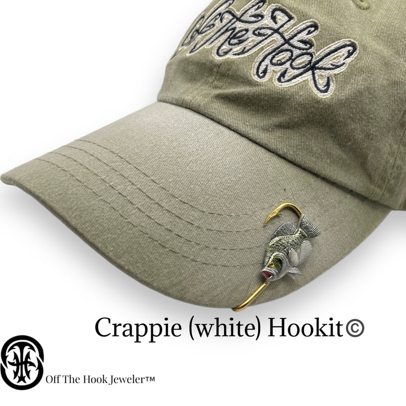 May include: A green baseball cap with the text "Off The Hook" embroidered on the front. A white crappie fish with a gold hook is attached to the cap.