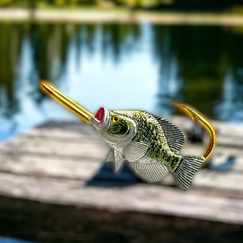 May include: A gold fishing lure shaped like a crappie fish with a red mouth and green and silver scales.