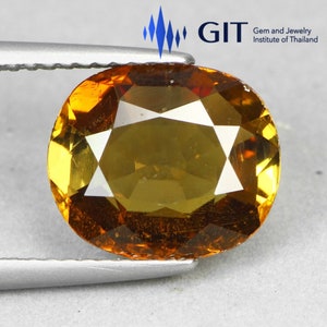 Puede incluir: Una piedra preciosa de corte ovalado con un tono naranja dorado profundo y superficie facetada, sostenida por pinzas de metal plateado. El logotipo del GIT Gem and Jewelry Institute of Thailand es visible en la parte superior.