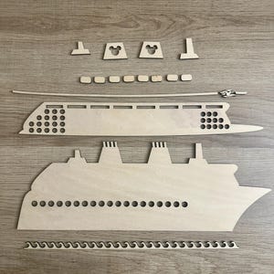 Pode incluir: Kit de artesanato de madeira para construir um navio de cruzeiro. O kit inclui o casco do navio, o convés e outros detalhes, bem como um conjunto de peças em forma de Mickey Mouse para as chaminés do navio.