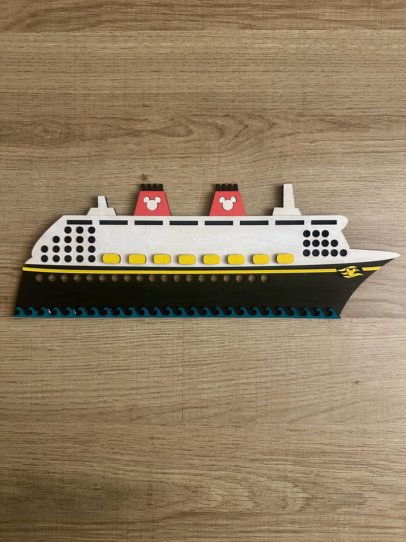 May include: A white and black cruise ship with yellow accents and red Mickey Mouse ears on the top. The ship is on a wood grain background.