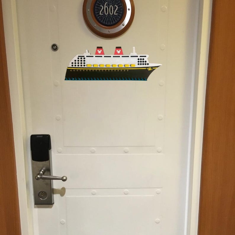 May include: White door with a silver door handle and a black digital lock. The door has a round porthole with the number 2602 on it. A white and black cruise ship sticker is on the door.