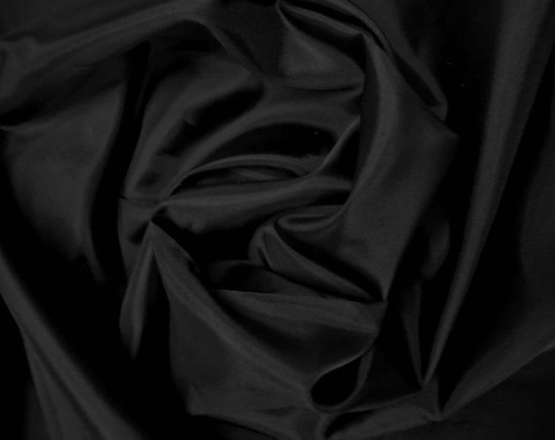May include: Black fabric with a smooth, silky texture. The fabric is draped and folded, creating soft, flowing curves.