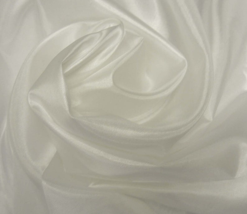 May include: White satin fabric with soft, flowing folds. The fabric is smooth and silky to the touch.