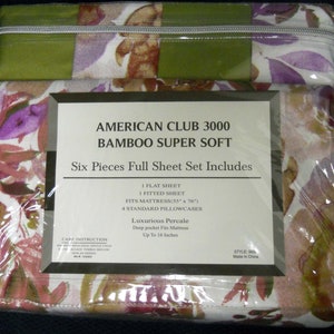Op de afbeelding: Een zesdelig volledig lakengoedset in een bloemenpatroon met groene, paarse en roze accenten. De verpakking bevat de tekst "American Club 3000 Bamboo Super Soft" en beschrijft dat het lakengoedset een plat laken, een hoeslaken en vier standaard kussenslopen bevat. Het lakengoedset is gemaakt van luxe perkal en past op matrassen tot 40 cm diep. Het lakengoedset is gemaakt in China.