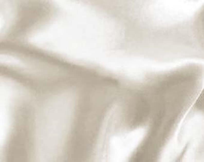 May include: Close-up of a cream-colored fabric with a silky sheen. The fabric has soft folds and a smooth texture, reflecting light and creating highlights and shadows. The material appears to be lightweight and flowing.