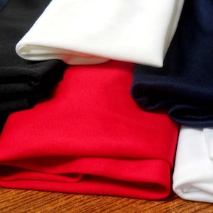 May include: Four rolls of fabric in different colors: black, white, red, and navy blue. The fabric is folded and stacked on a wooden surface.