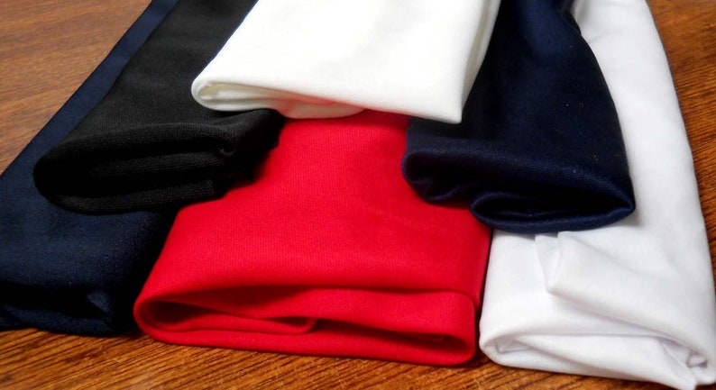 K&ouml;nnte beinhalten: Vier Rollen Stoff in verschiedenen Farben: Schwarz, Wei&szlig;, Rot und Marineblau. Der Stoff ist gefaltet und auf einer Holzoberfl&auml;che gestapelt.