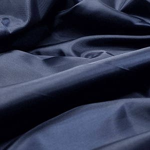 May include: A close-up of a dark blue fabric with a smooth, silky texture. The fabric is folded and draped, creating soft folds and curves.
