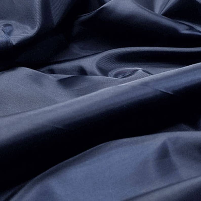 May include: A close-up of a dark blue fabric with a smooth, silky texture. The fabric is folded and draped, creating soft folds and curves.