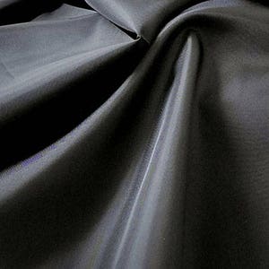 May include: Black fabric with a smooth, silky texture. The fabric is folded and draped, showing its sheen and drape.