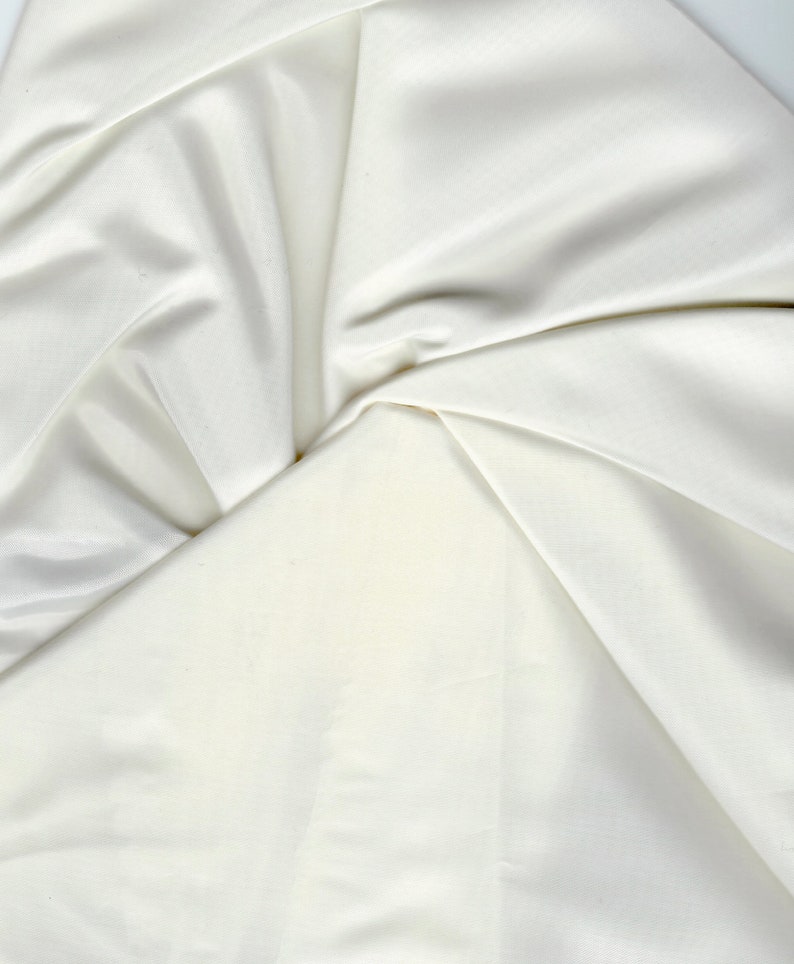 May include: A close-up of a white fabric with soft folds and wrinkles. The fabric is smooth and silky, with a subtle sheen.